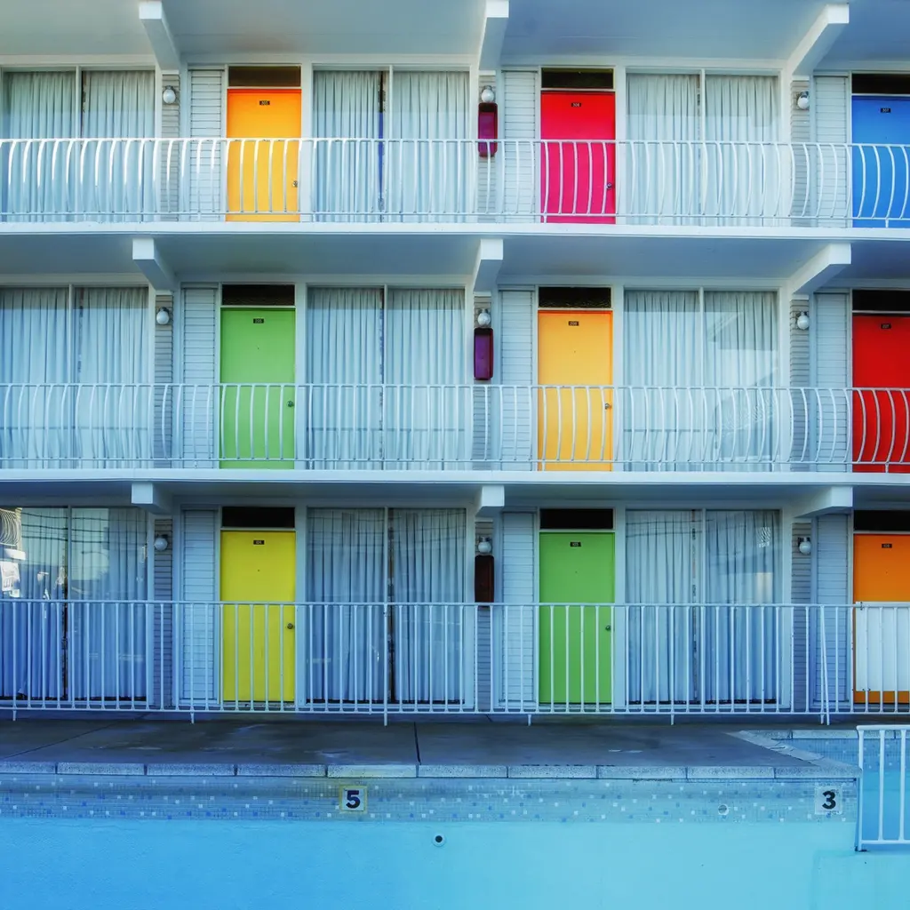 Brightly colored motel-room doors and exterior walkways beside a swimming pool.
