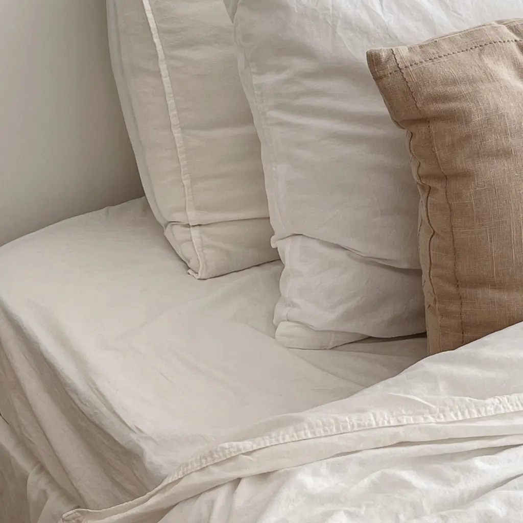 White bed sheets, quilted bedding and pale pillows arranged on a bed.