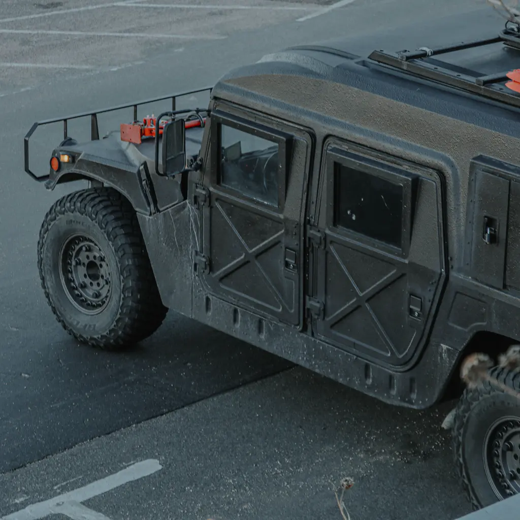 An olive-drab military Humvee with armored doors parked on pavement.