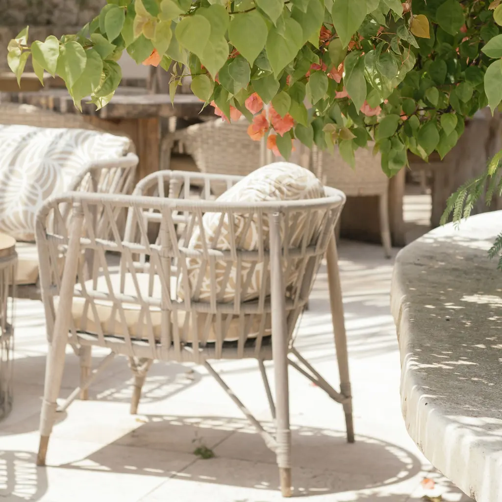 Woven outdoor armchairs and a round patio table beneath flowering greenery.