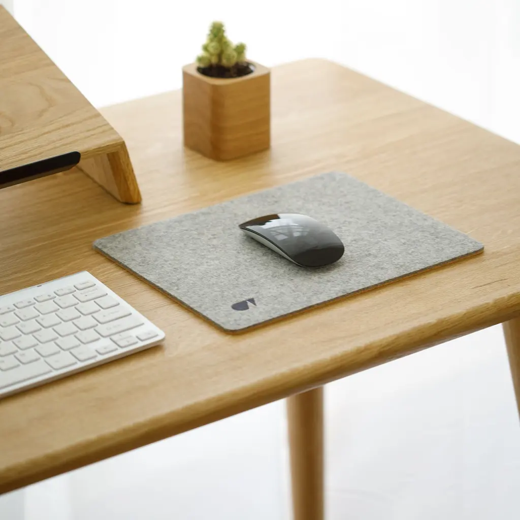 A computer mouse on a gray mat beside a white keyboard on a wooden desk.