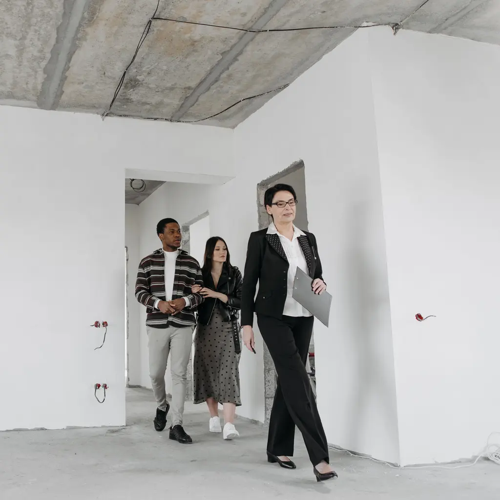A real estate professional showing two prospective buyers an unfinished residential room.