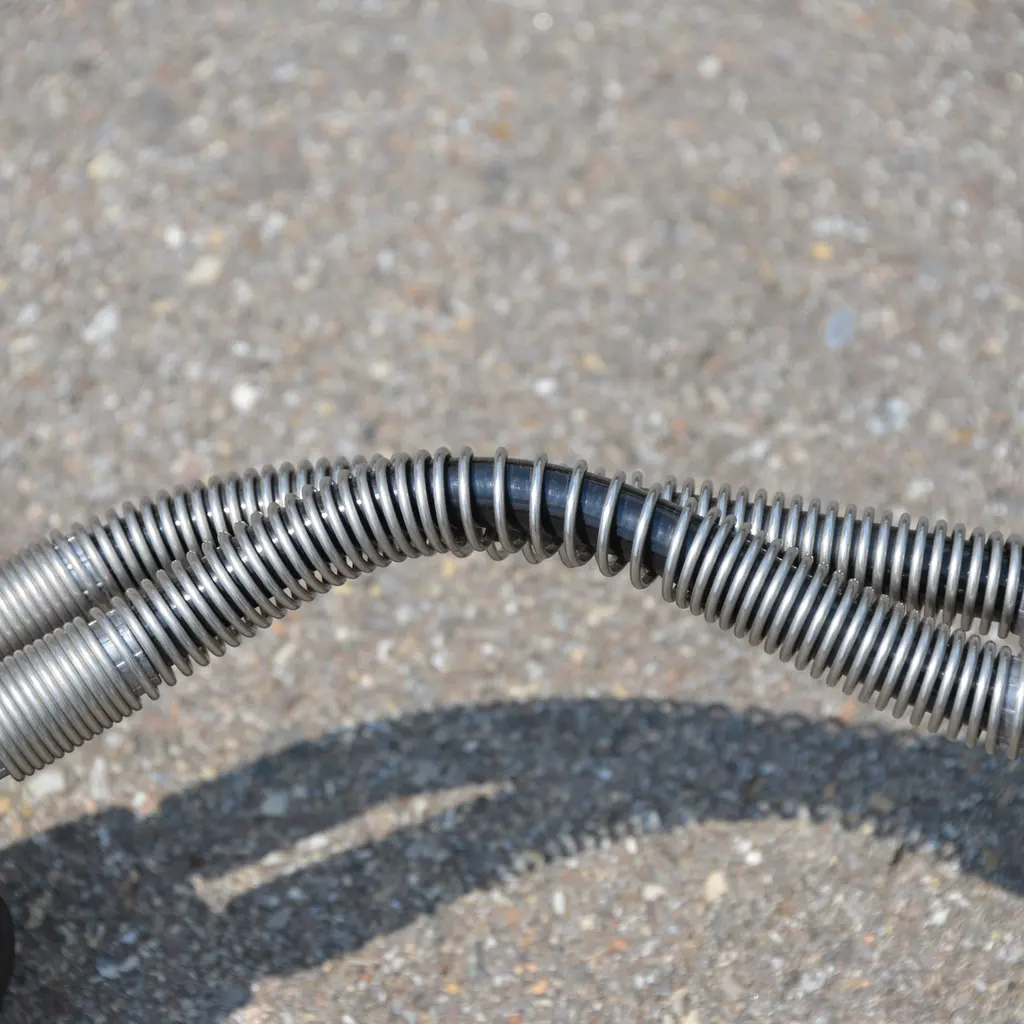 A flexible black pressure hose protected by a coiled steel anti-kink spring.