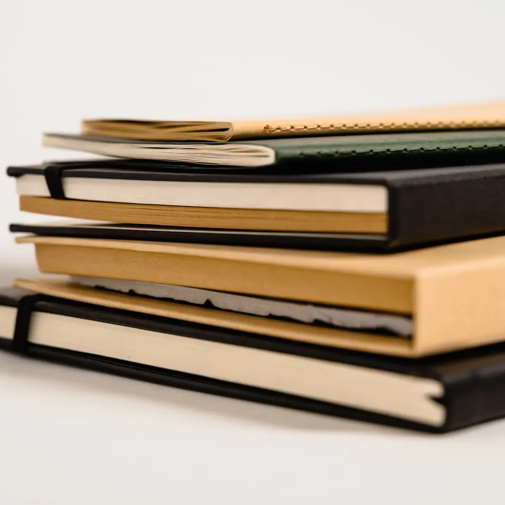 A stack of plain notebooks with colored covers and visible page blocks.