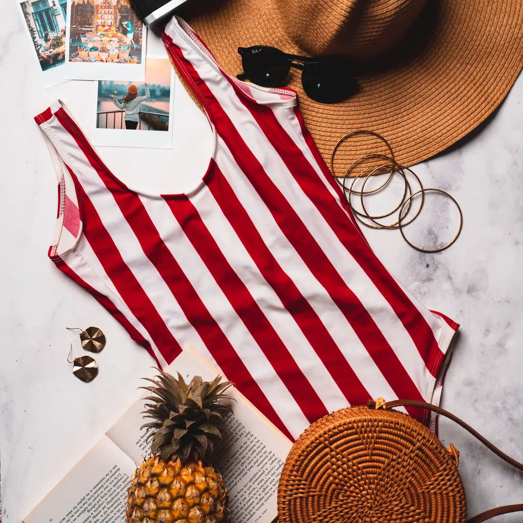 A red-and-white striped one-piece swimsuit laid flat among beach accessories.