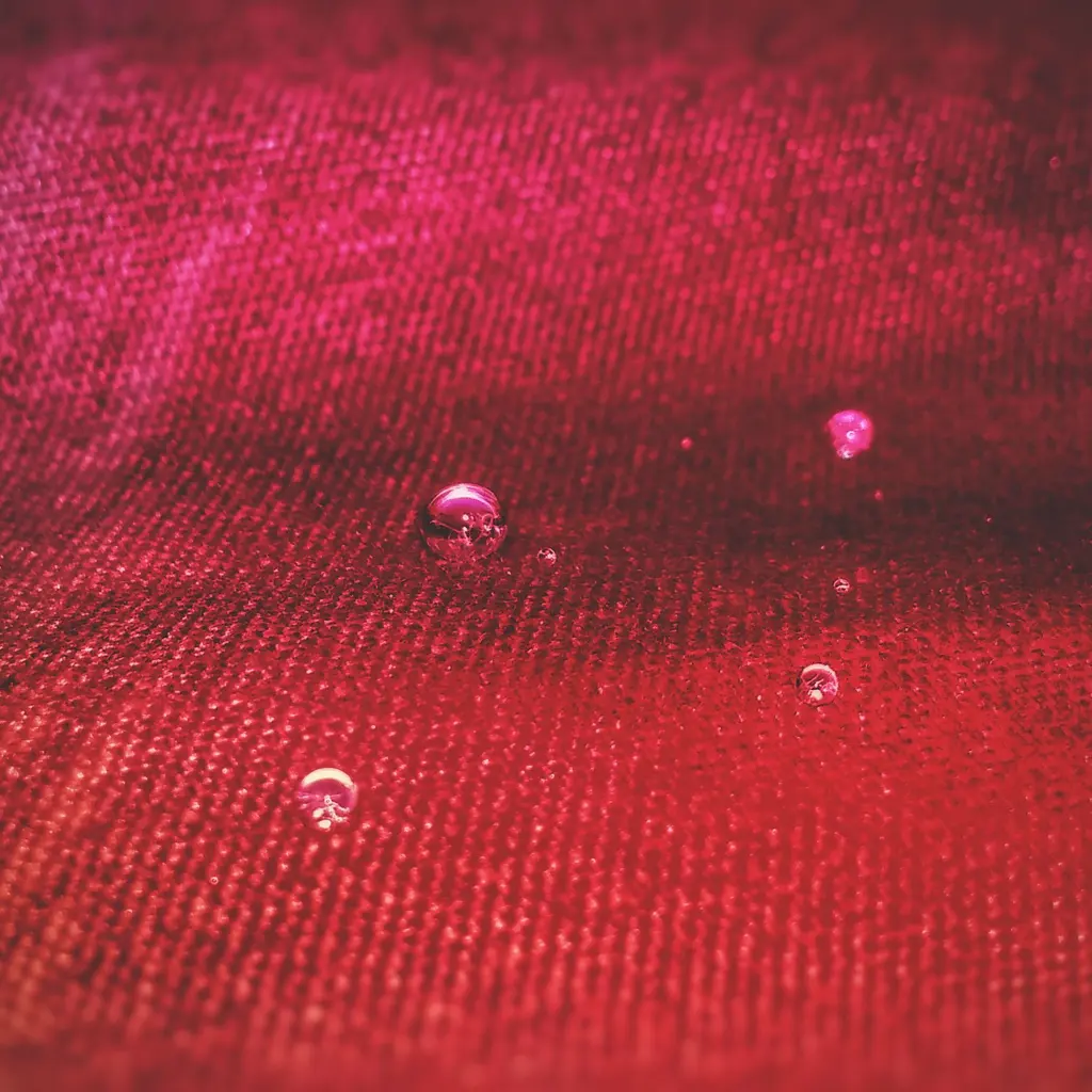 Water droplets beading on the textured surface of red woven fabric.