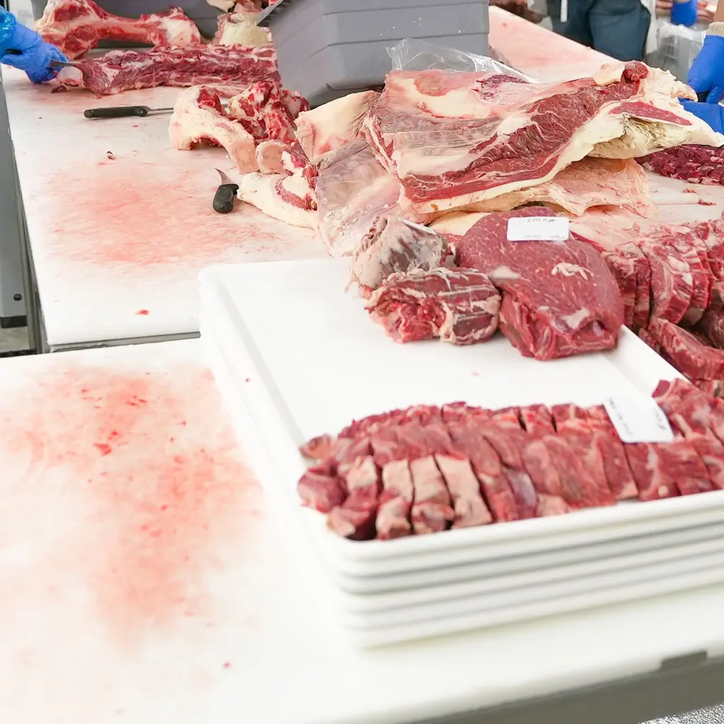 Cut meat, knives and stacked trays arranged on tables in a meat-processing room.