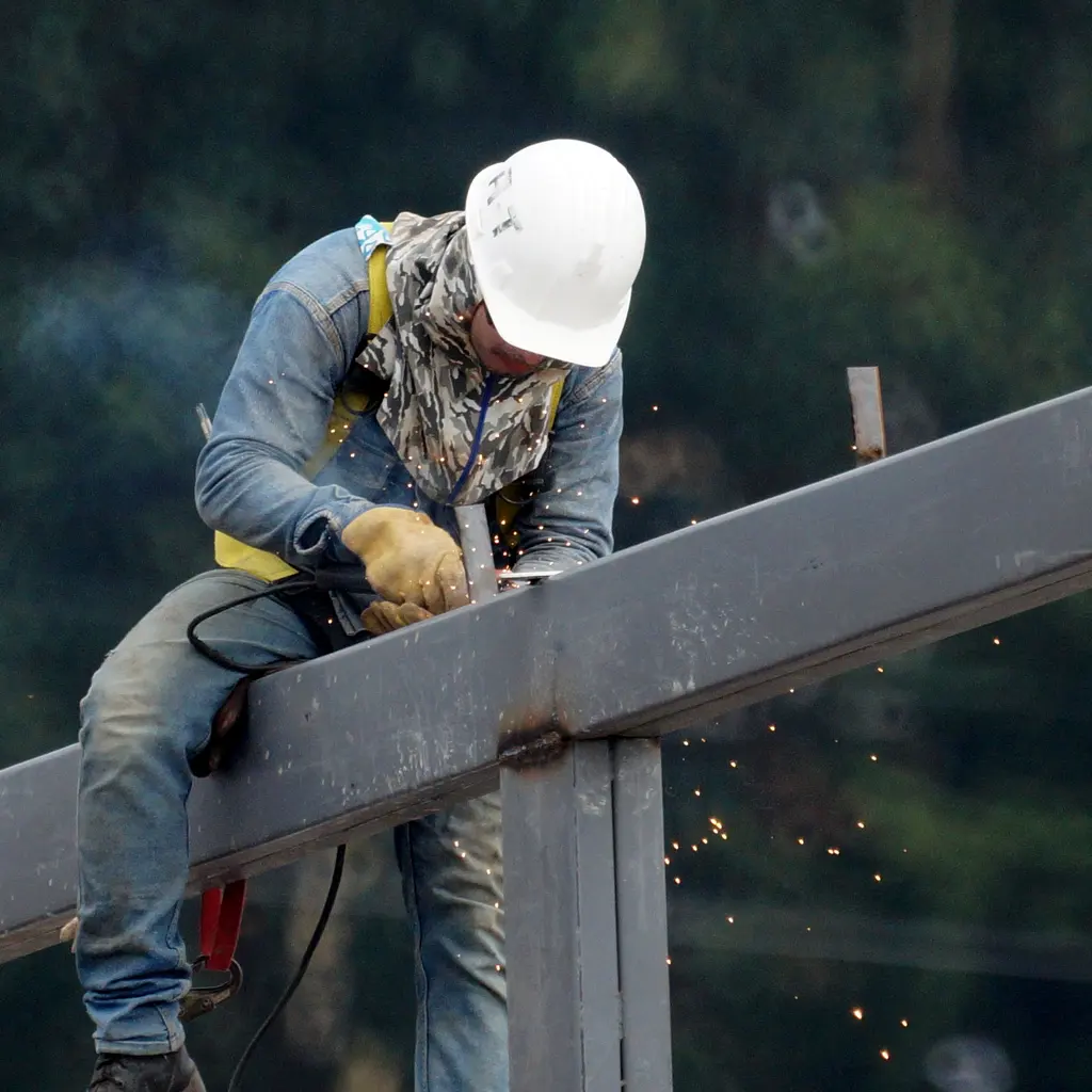 Worker welding a steel beam connection on an erected building frame.
