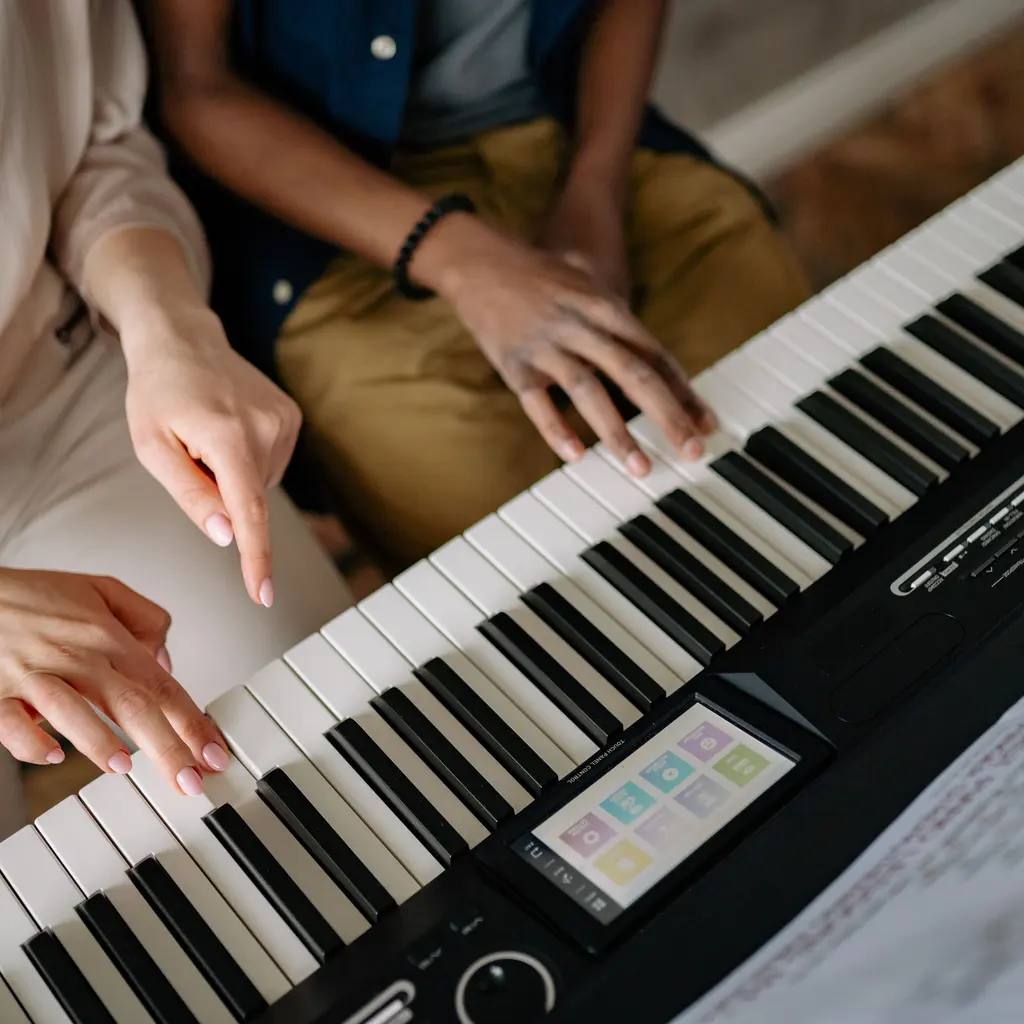 Hands playing a digital keyboard while another hand points toward the keys.