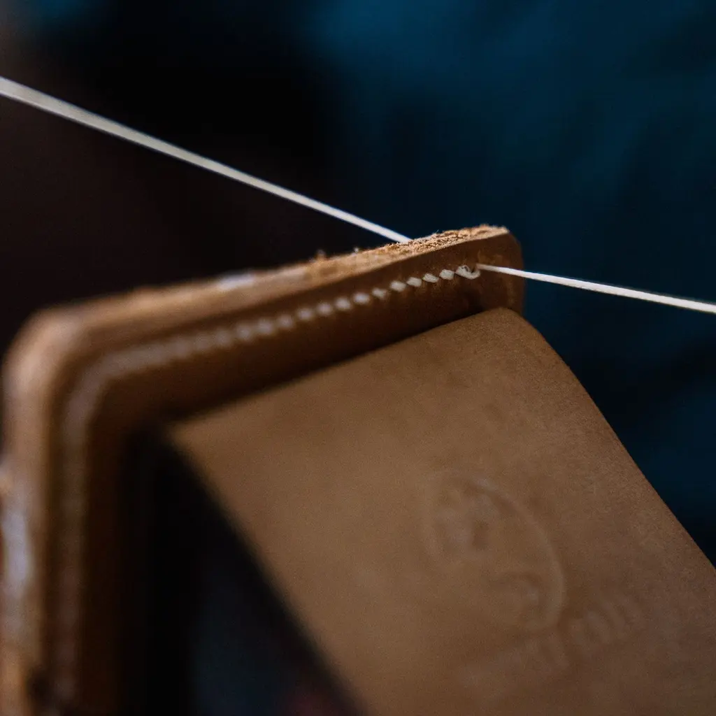 White stitching thread extends from the edge of a leather wallet held in a clamp.