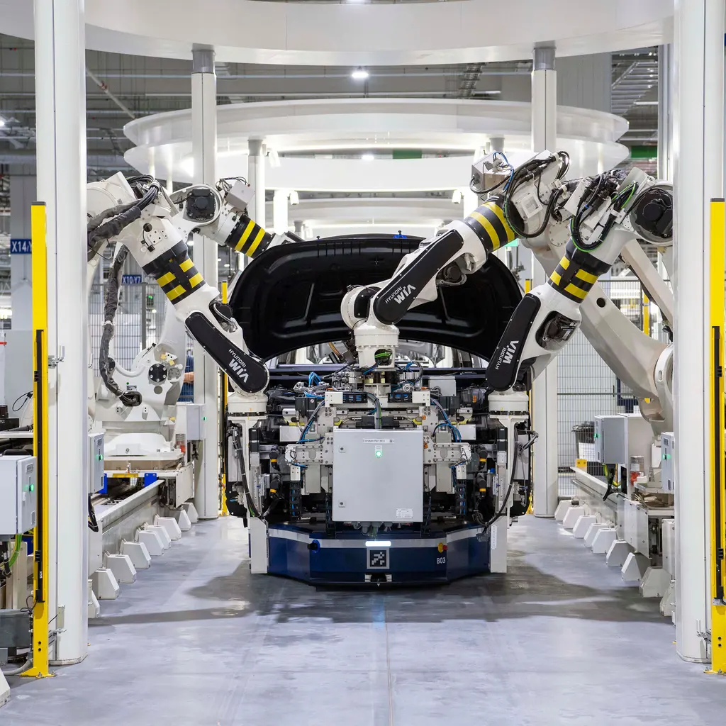 Robotic arms surround a vehicle panel on a fixture in an automated assembly cell.