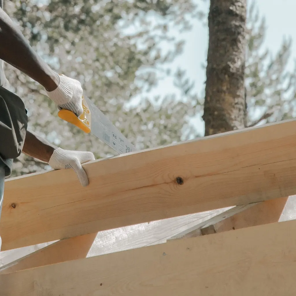 Gloved hands using a manual saw on a timber member in a wooden framework.