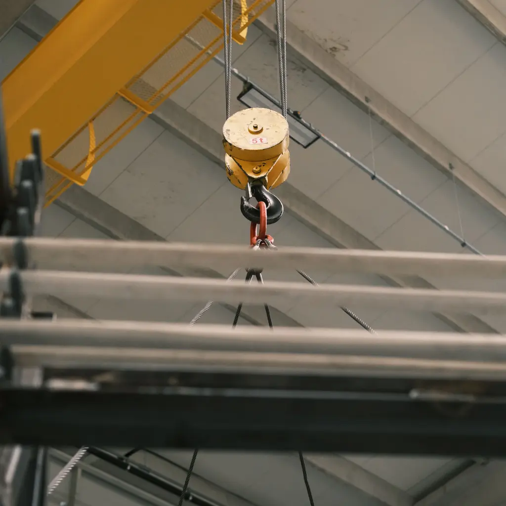 An overhead crane hook block and connected wire-rope rigging inside an industrial building.