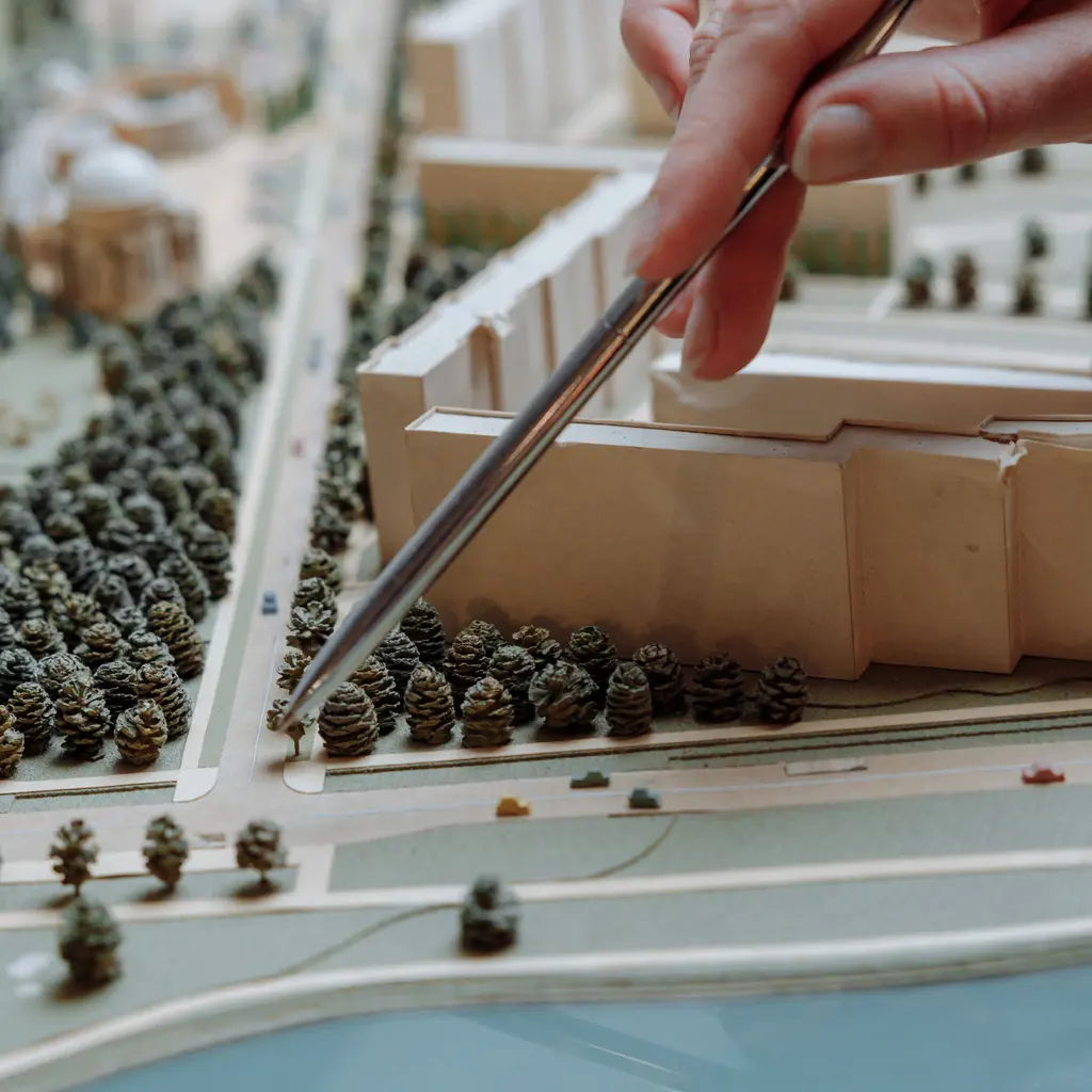 A hand holds tweezers over an architectural scale model.