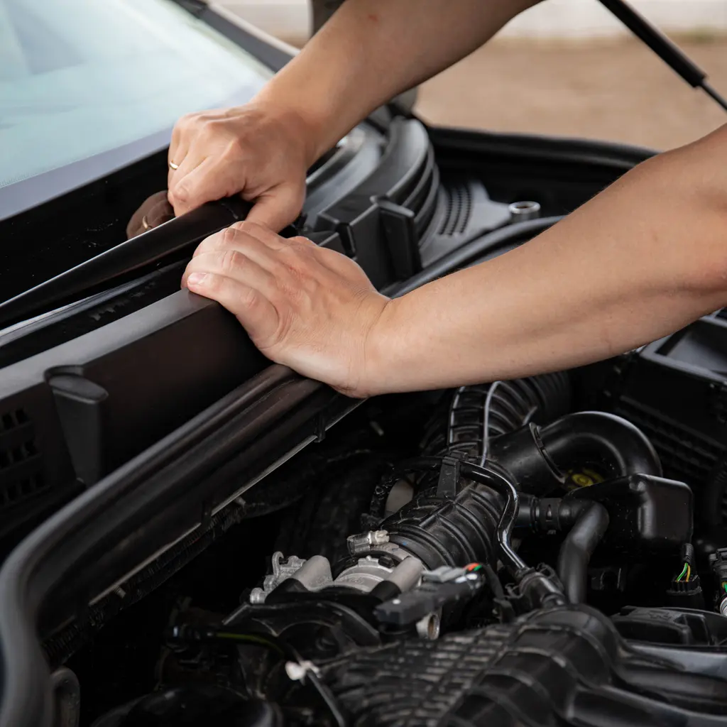 Hands working at a car's windshield-wiper area.