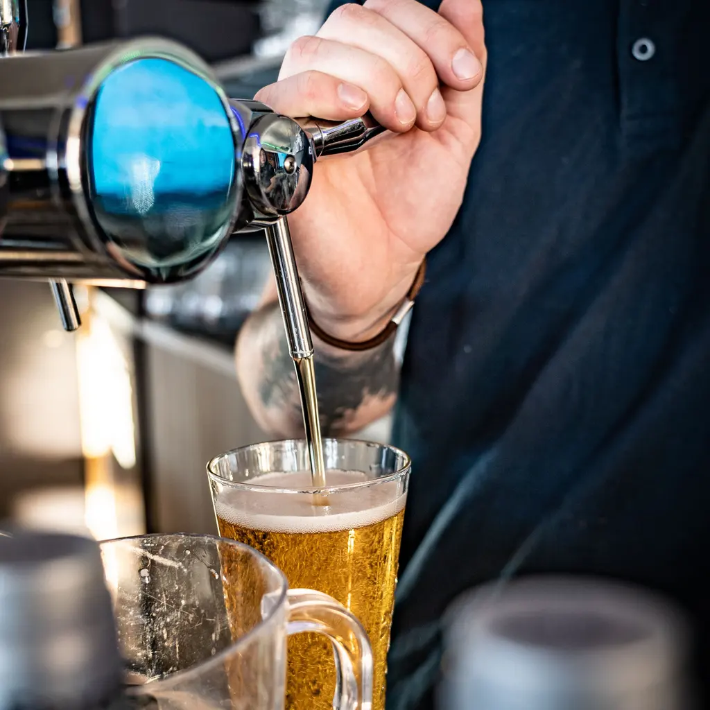 A bartender pulls a draft tap to fill a tall glass with beer at the bar.