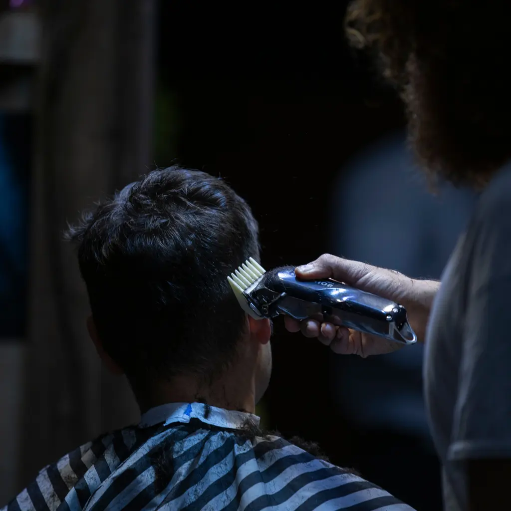 A barber using clippers with a comb guard on a client's hair.