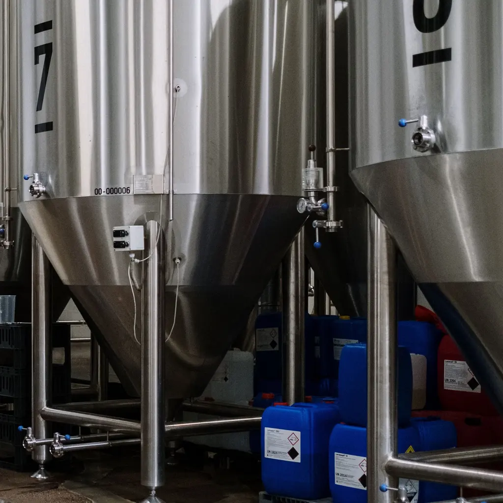 Stainless-steel fermentation tanks, valves and pipework inside a brewery.