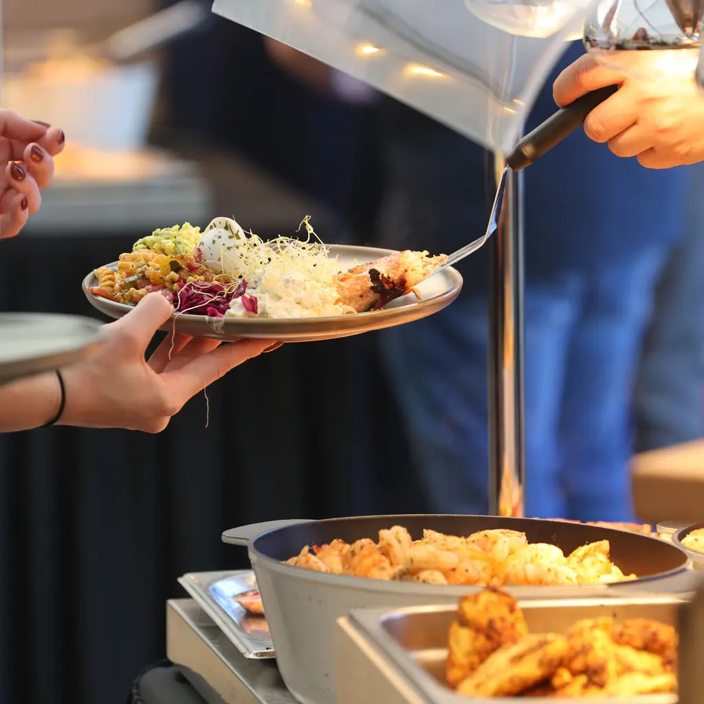 Hands hold a plate and serving utensil at a buffet counter.