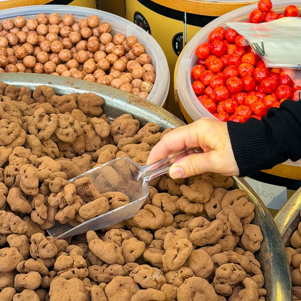 A hand holds a scoop in a tray of sweets.