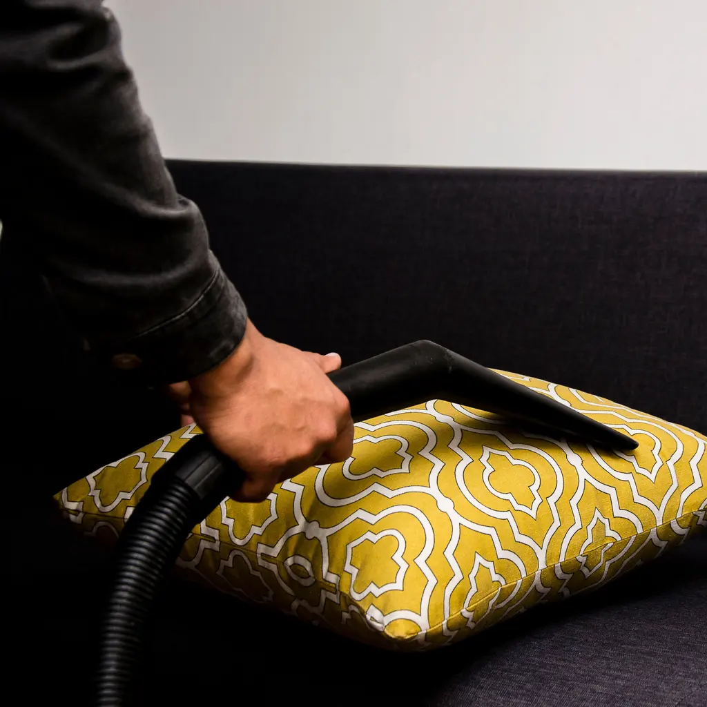 Vacuuming a patterned cushion on a sofa.