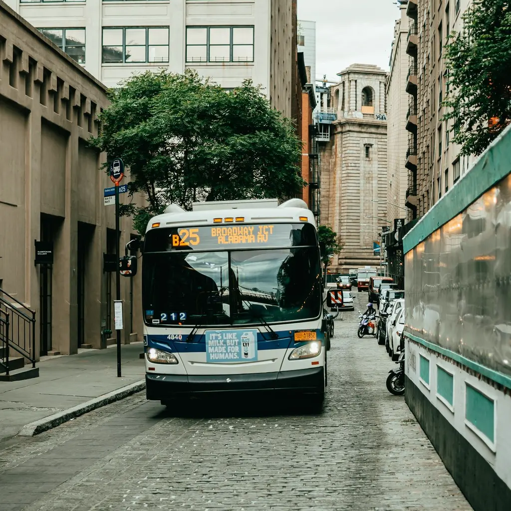 A city bus and bus-stop sign on a narrow street lined with buildings.