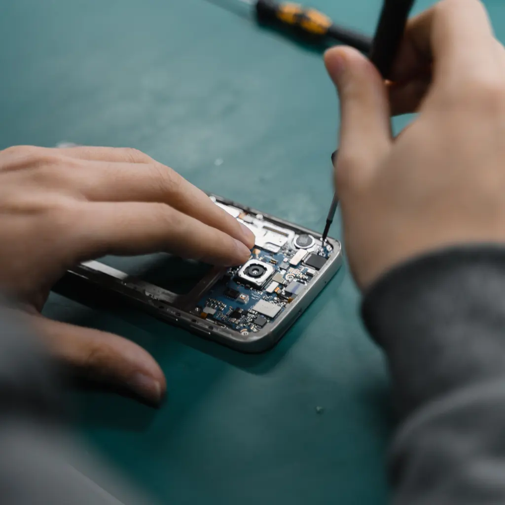 Hands using a precision screwdriver inside an open smartphone.