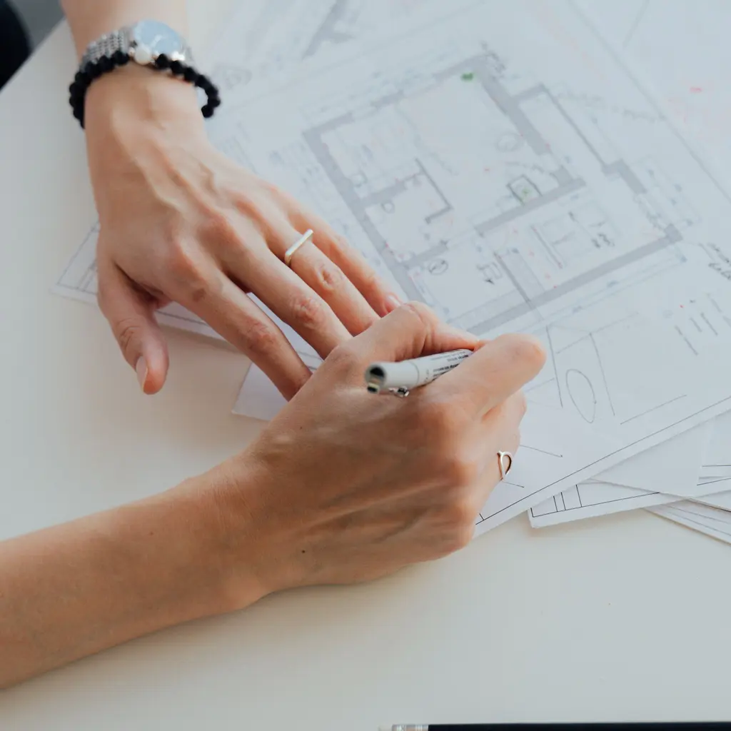 Hands hold a pen over a printed floor plan.