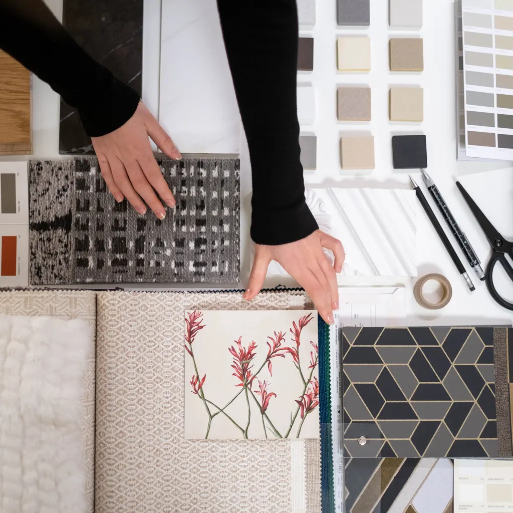 Hands compare fabric and finish samples with color swatches on an interior-design worktable.
