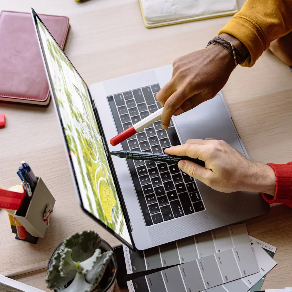 Hands point at a landscaped site plan on a laptop beside color samples.