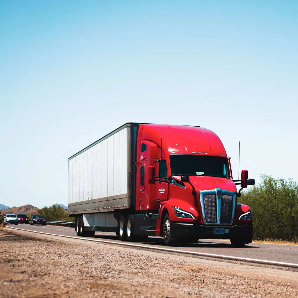 A red sleeper-cab tractor pulls an enclosed freight trailer along a highway.
