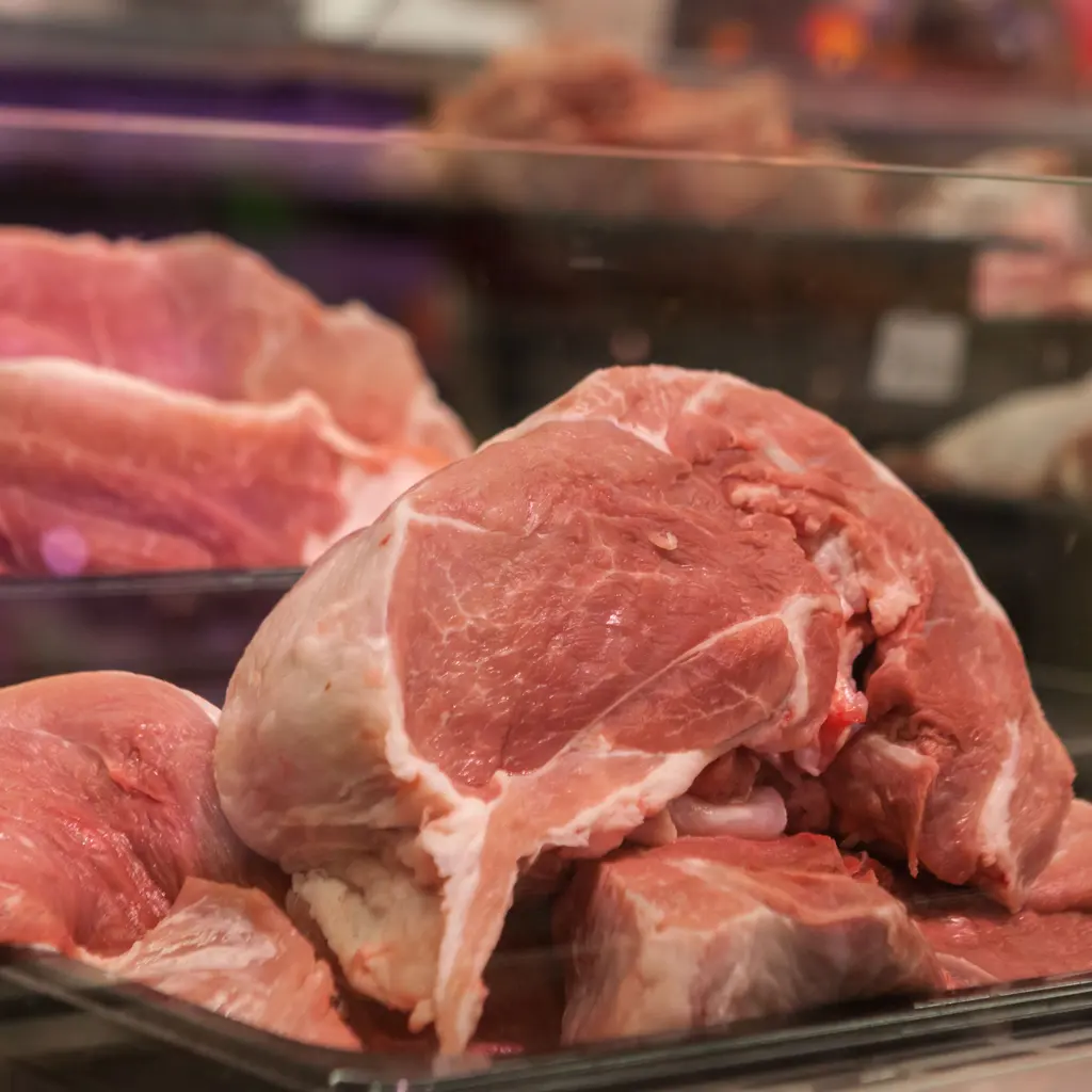 Raw cuts of meat arranged behind a butcher counter's glass display.