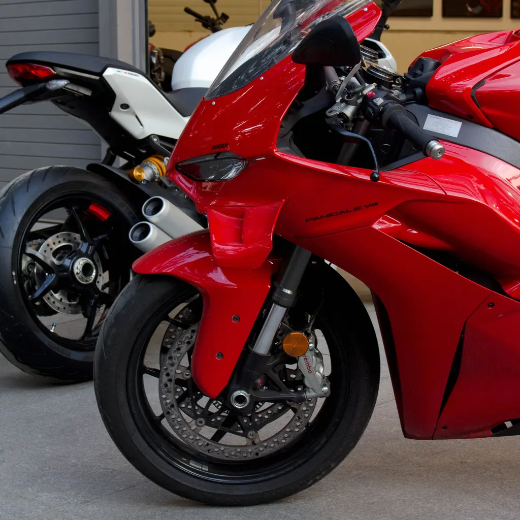 The front fairing and wheel of a red sport motorcycle beside another bike in a showroom.