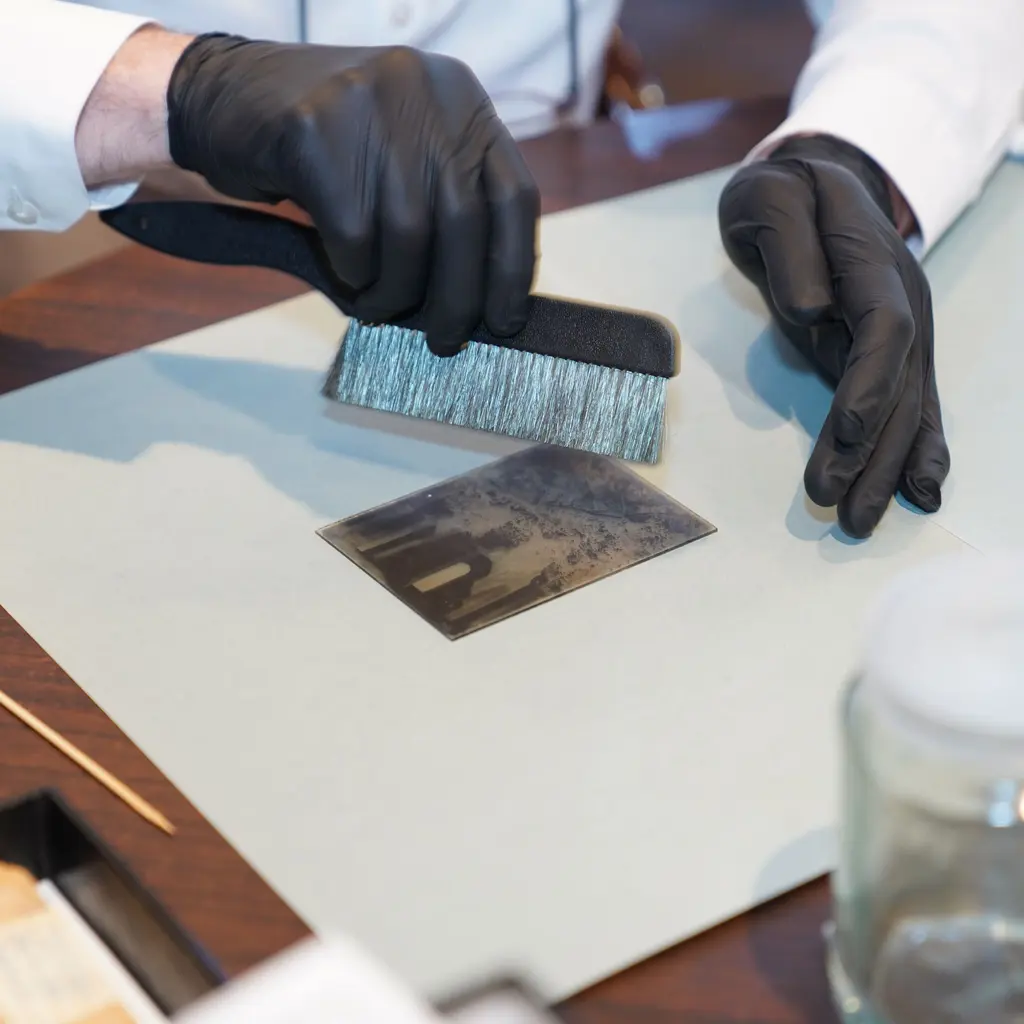 A gloved hand holds a brush above a photograph on a worktable.