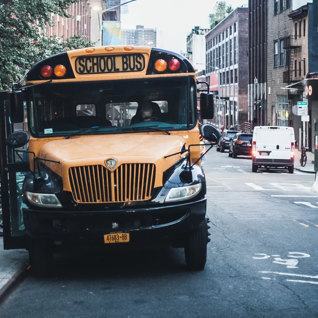 A yellow school bus stands at a city curb with its passenger door open.