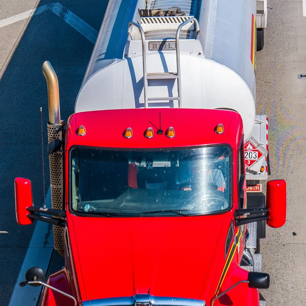 Overhead view of a red tractor cab and the rounded front of its tank trailer on a road.