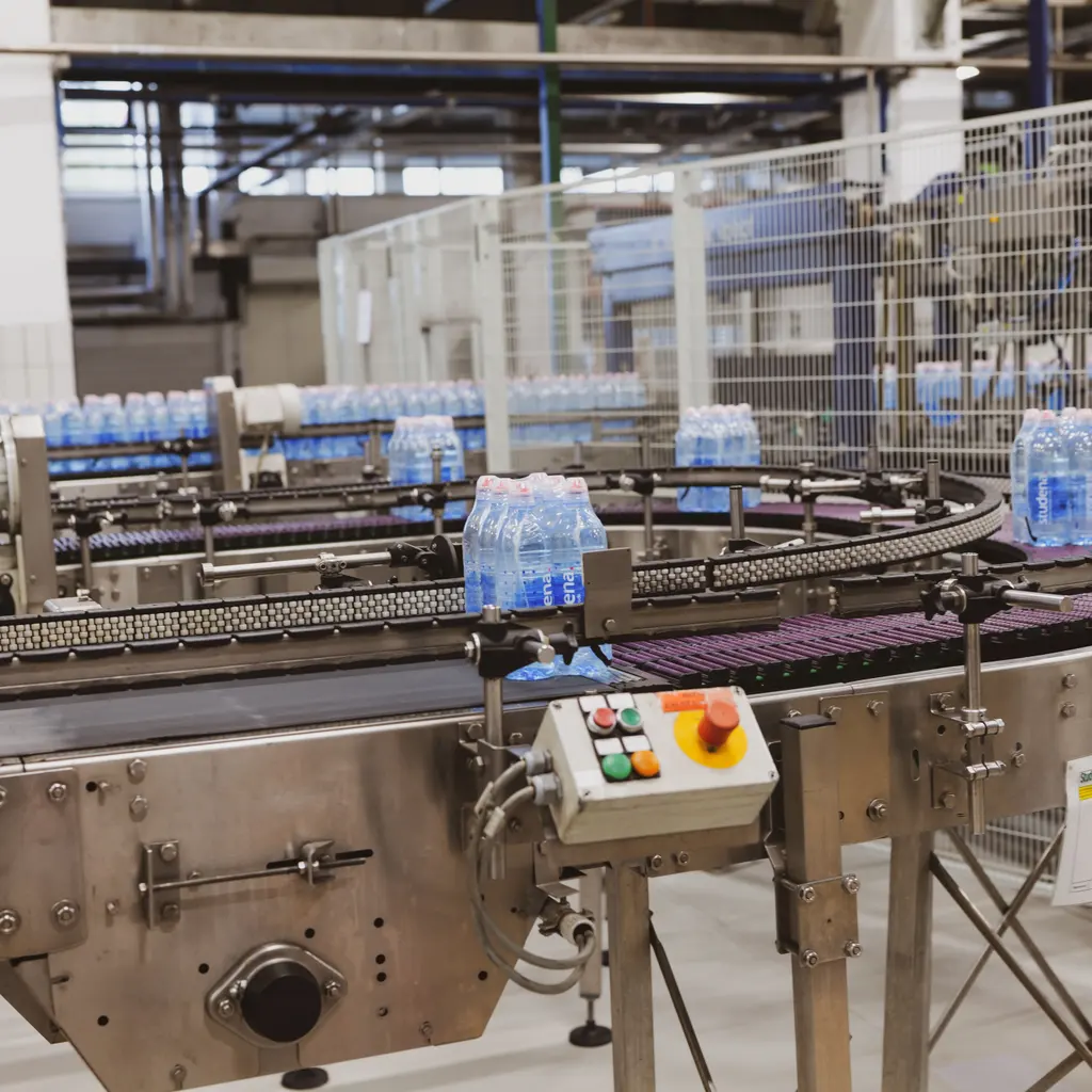 Shrink-wrapped packs of water bottles sit on a factory conveyor.