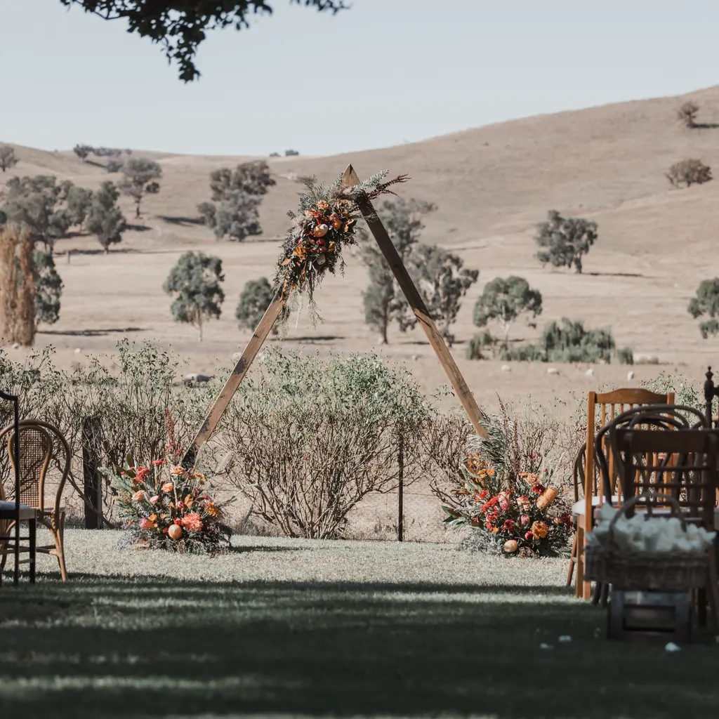 Outdoor wedding seating facing a triangular floral arch.