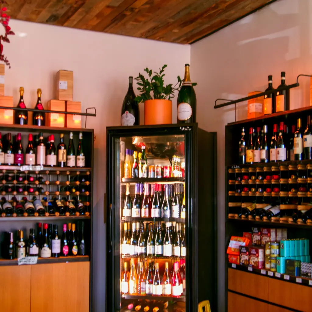 Wine bottles fill retail racks and a glass-door cooler in a small wine shop.
