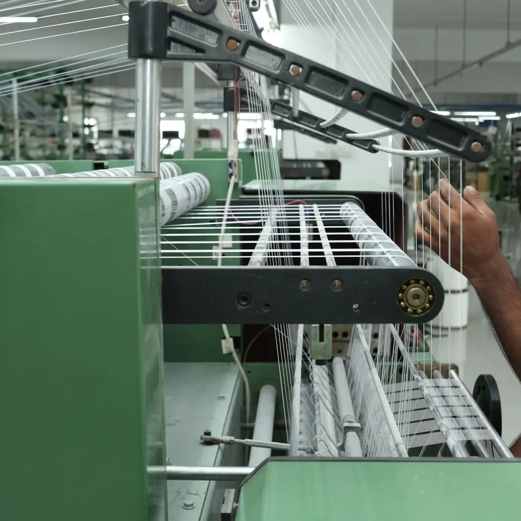 Parallel yarns run through guides as a worker adjusts threads on a textile machine.