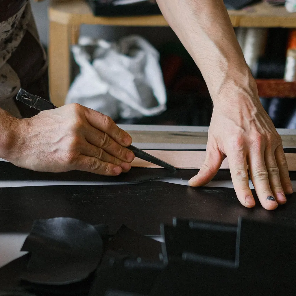 An artisan cuts black leather along a pattern on a worktable.