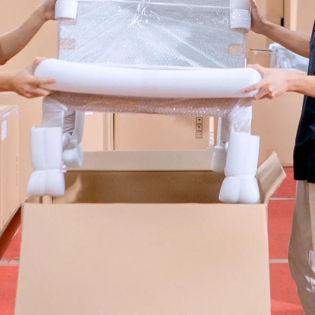 Hands lowering a foam-protected chair into an open shipping carton.