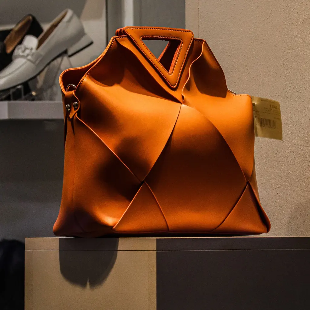 An orange handbag is displayed on a stand in a boutique.