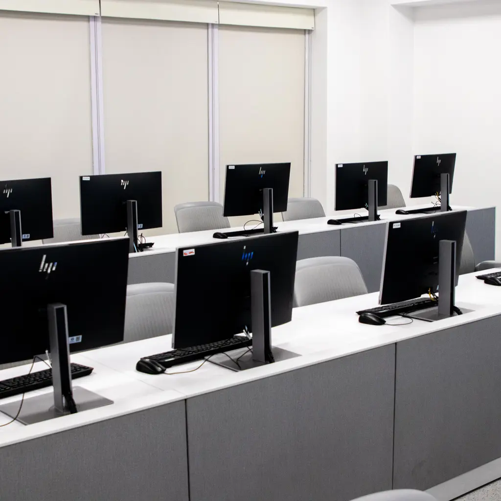 Rows of desktop computers and chairs in an empty classroom computer lab.