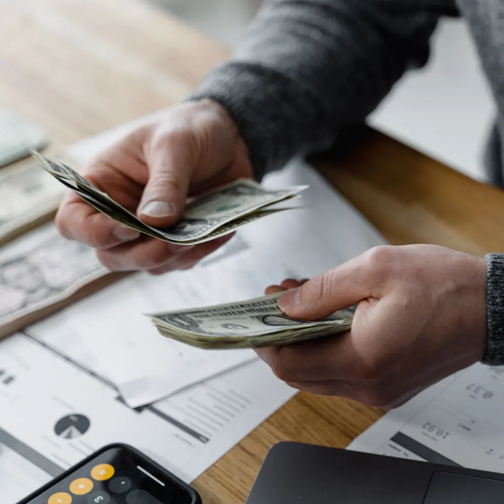 Hands counting U.S. dollar banknotes beside financial charts and a calculator.