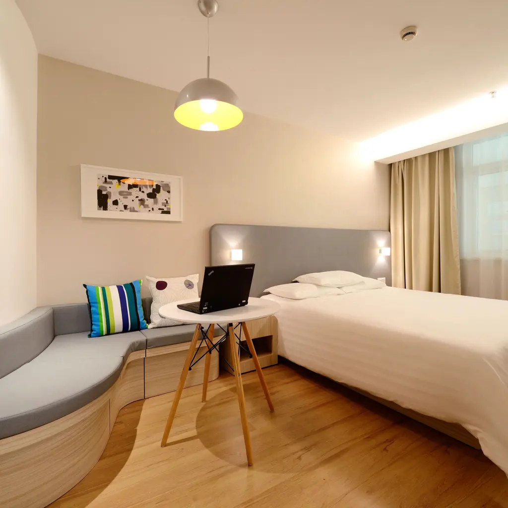 Bright guest room with a made bed, seating area and a laptop on a small table.