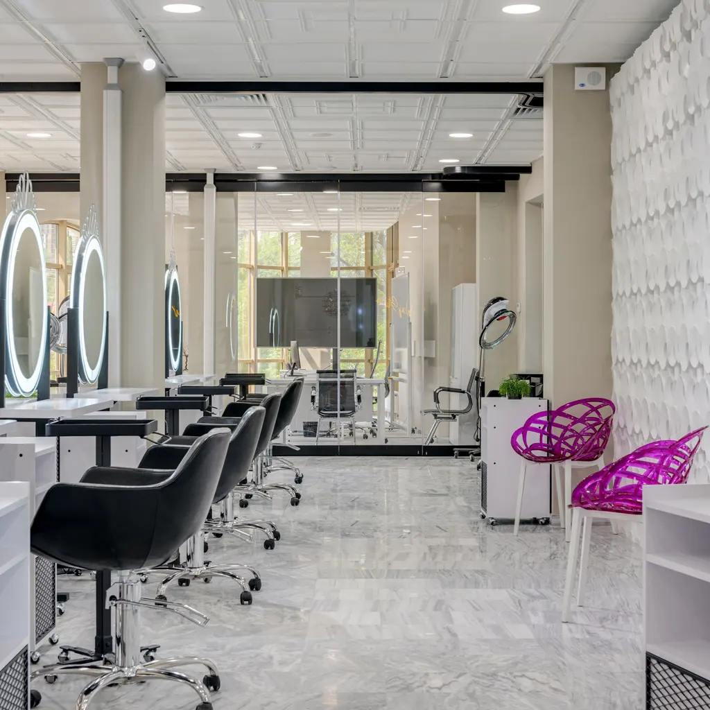 Empty salon styling stations with hydraulic chairs, counters and illuminated mirrors.