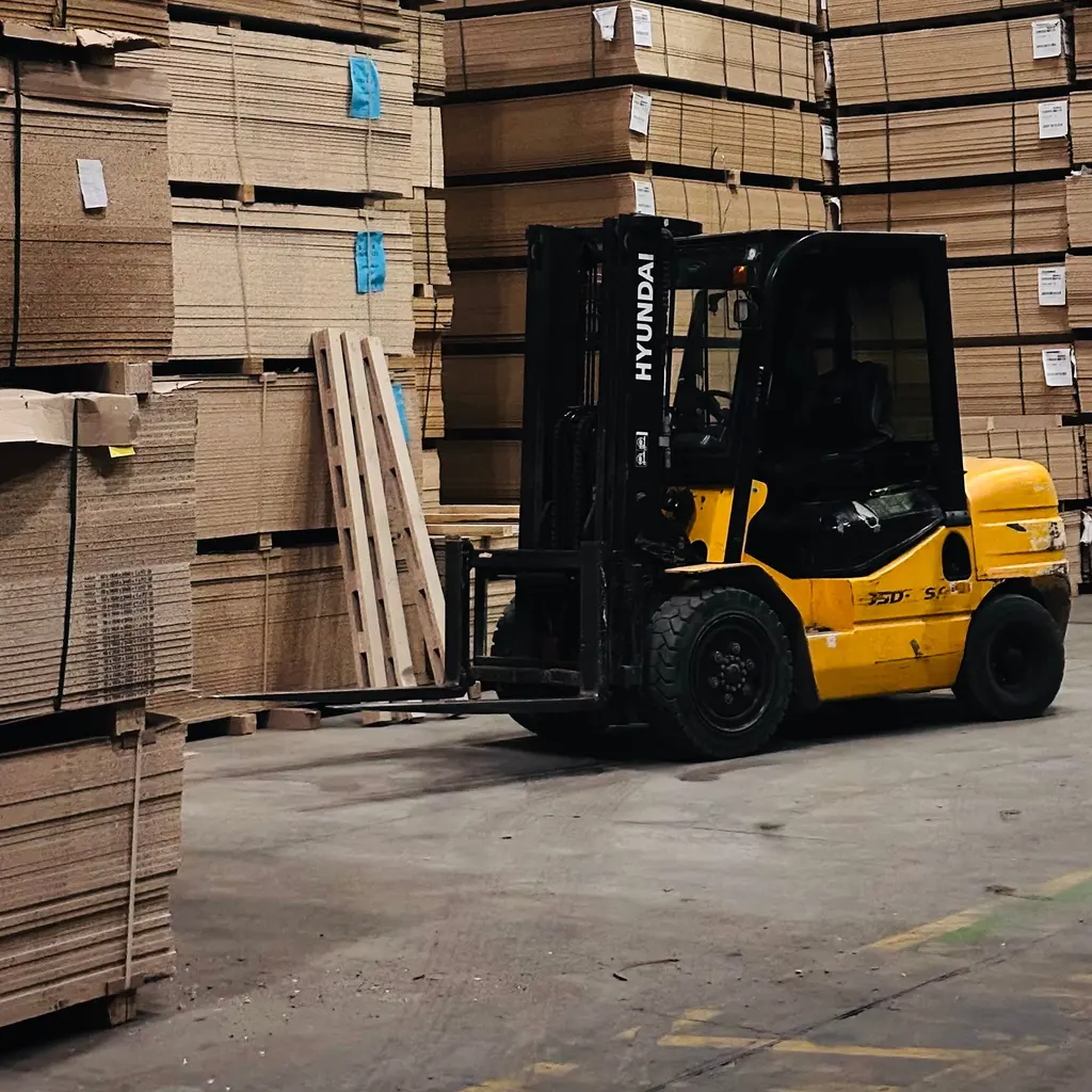 A forklift parked beside palletized stacks of cardboard inside a warehouse.