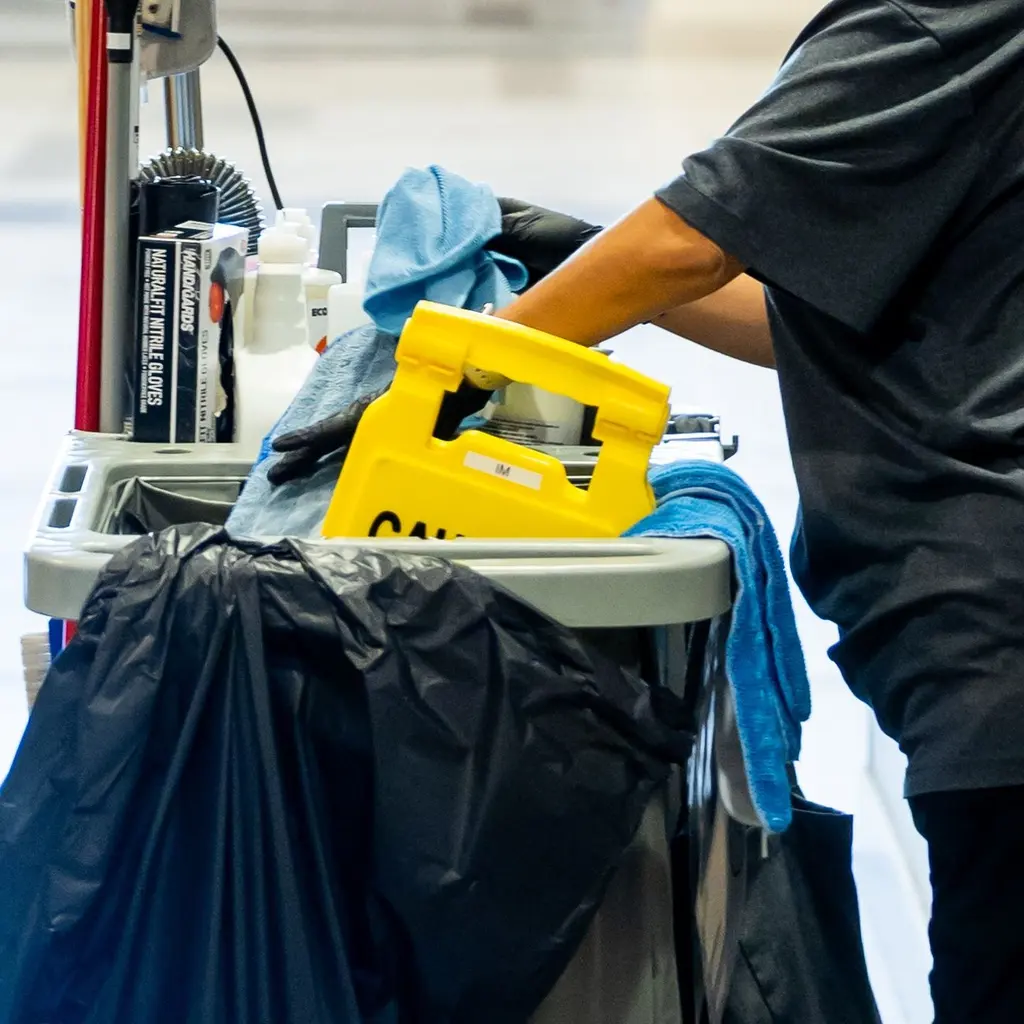 Gloved hands handling cloths among cleaning supplies on a janitorial cart.