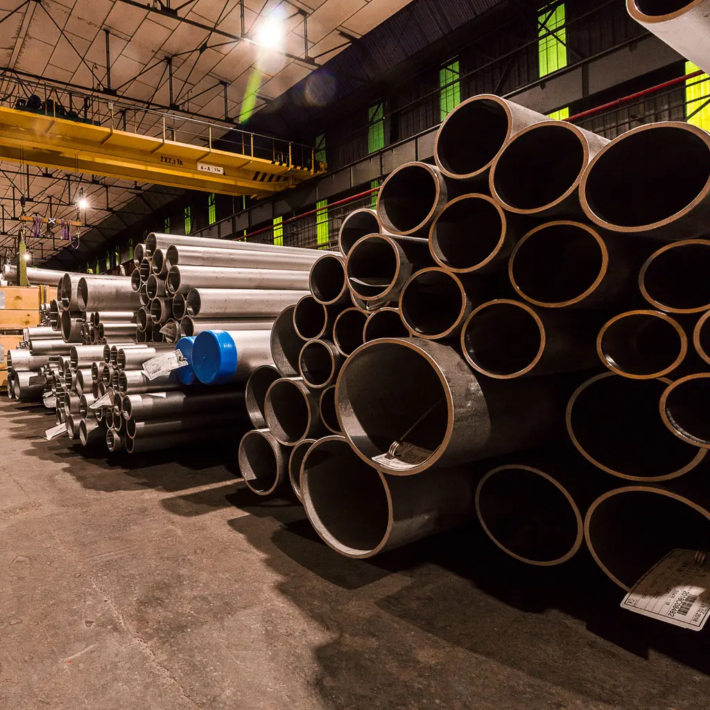 Stacks of metal pipes in different sizes fill a warehouse storage bay.